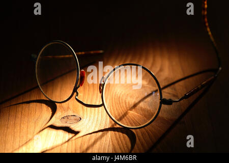 Primo piano di vecchi occhiali con lunga ombra sulla superficie di legno Foto Stock