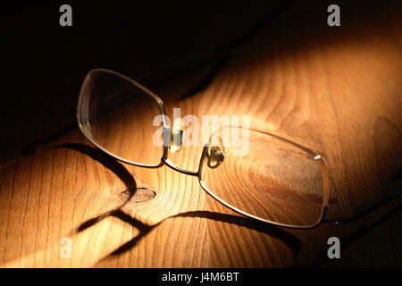Primo piano di occhiali con lunga ombra sulla superficie di legno Foto Stock