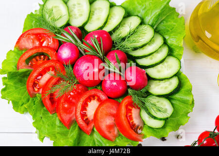 Tritate grossolanamente cetriolo fresco, pomodoro, ravanello e lattuga - insalata fresca. Il concetto di mangiare sano, dieta, il vegetarianismo Foto Stock