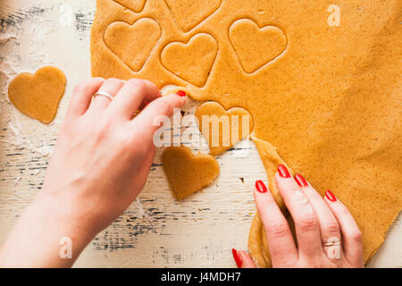 Le mani della donna la separazione di cuore le forme tagliate dalla pasta biscotto Foto Stock