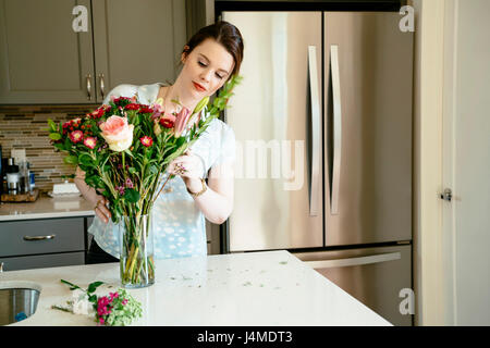 Donna disponendo dei fiori in cucina domestica Foto Stock