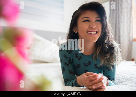 Sorridente razza mista donna posa sul letto Foto Stock