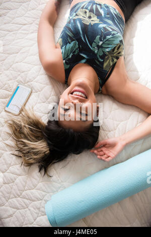 Sorridente razza mista donna posa sul letto appoggiato dopo allenamento Foto Stock