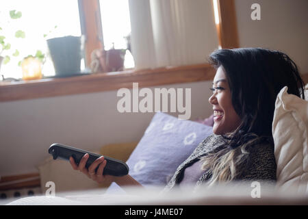Sorridente razza mista donna tenendo premuto il telecomando e guardare la televisione Foto Stock