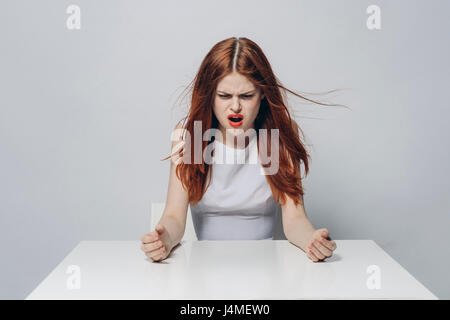Arrabbiato Caucasian donna seduta al tavolo di vento Foto Stock