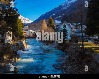 Gelido fiume che scorre attraverso il villaggio di Andermatt svizzera con neve montagne sullo sfondo Foto Stock