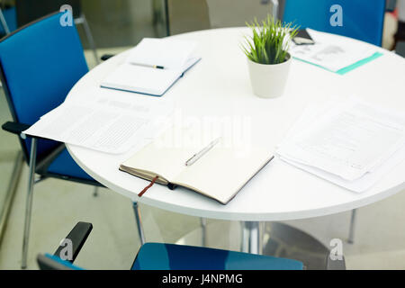 Oggetti per business meeting sulla tavola rotonda con diverse sedie vuote nelle vicinanze Foto Stock