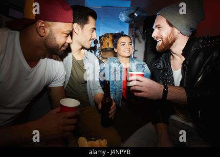 Contemporary giovane uomo in giacca di pelle appeso fuori con gli amici a tarda notte partito, chiacchierare e bere birra Foto Stock