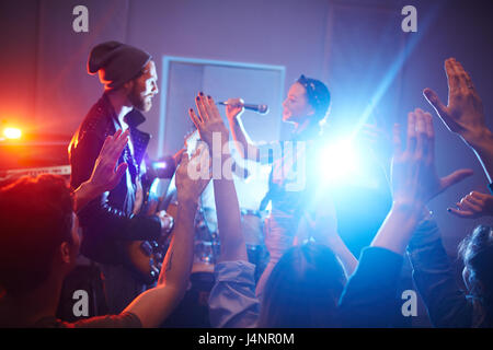 Locali del rock band di eseguire musica sul palcoscenico di urban club con la folla che acclamava e ballo persone partying, alzando le mani Foto Stock