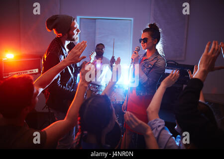 Cool band canto sul palco di urban club con la folla che acclamava e ballo persone partying, alzando le mani Foto Stock