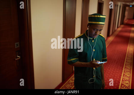 Ritratto di afro-americano di portantino ascoltando la musica nella hall dell'hotel, in pausa dal lavoro Foto Stock