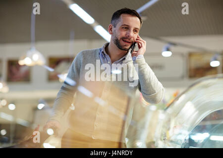 Ritratto di bello uomo maturo facendo la spesa nel supermercato: chiamata di sua moglie chiedendo cosa acquistare Foto Stock