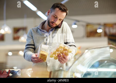 Ritratto di confuso uomo di mezza età facendo la spesa nel supermercato: chiamata di sua moglie chiedendo cosa dessert a scelta Foto Stock