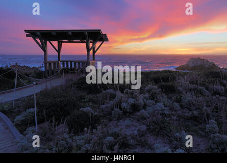 Nuvole drammatico al tramonto dietro un pubblico passeggio e gazebo in stato di Asilomar Beach in Pacific Grove sulla penisola di Monterey in California Foto Stock