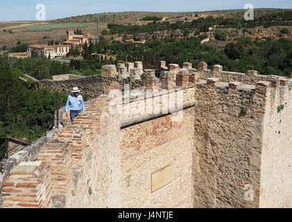 Un uomo persona turistica con hat cappelli in cima a piedi lungo la parte superiore old antica pietra medievali storiche mura della città dentelli rovine a Segovia, Spagna Foto Stock