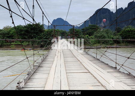 Vang Vieng, Laos-October 13, 2015: ragazzi locali sulle biciclette attraversare il ponte a pedaggio sezione 1 al di sopra del Nam Song river e interrompere la visione di un motoscafo sai Foto Stock