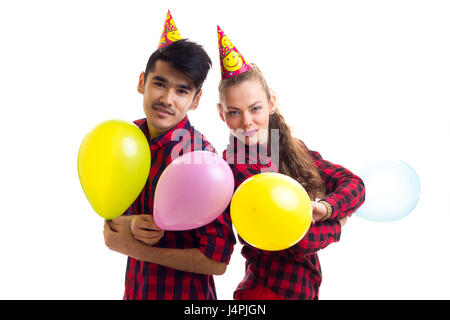 Giovane bella donna con lunga coda di cavallo di castagno e giovane uomo smartlooking in rosso plaid camicie con celebrando cappelli holding palloncini su sfondo bianco Foto Stock