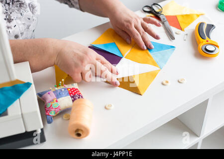 Ricamo trapuntatura a mano nella bottega di un sarto donna su sfondo bianco - le mani del sarto raccogliere dal desktop dei frammenti di tessuto colorato per patchwork sulla macchina da cucire. Foto Stock