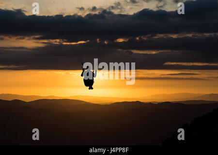 Bellissimo colpo di un parapendio silhouette volando verso il tramonto, con bellissimi colori arancione e toni scuri Foto Stock