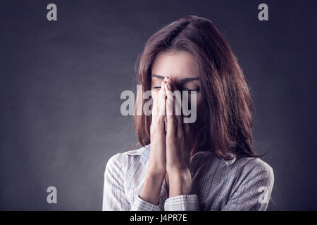 Giovane donna in lacrime nelle sue mani su sfondo nero Foto Stock