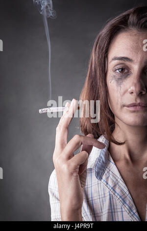 Una giovane donna con una sigaretta in mano su uno sfondo scuro Foto Stock