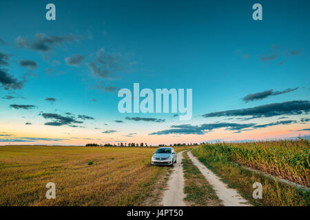 Gomel, Bielorussia - Agosto 13, 2016: Volkswagen Polo berlina auto parcheggio nei pressi di strade di campagna nel campo estivo. Sunset Sunrise Sky su uno sfondo nella soleggiata Eve Foto Stock