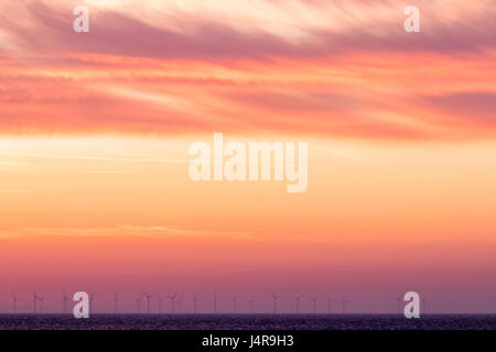Orange alba cielo sopra il Thanet per centrali eoliche offshore con fila di turbine onon all'orizzonte. Le turbine eoliche stagliano contro il luminoso cielo arancione. Foto Stock