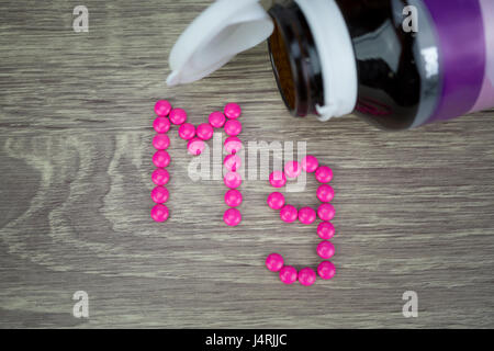 Pillole di rosa formando la forma per Mg alfabeto su uno sfondo di legno Foto Stock