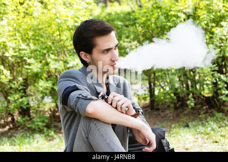 Considerato giovane imprenditore fuma una vape in un parco nel pomeriggio a molla Foto Stock