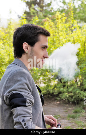 Ridendo giovane impreditore fumare una vape nel parco Foto Stock