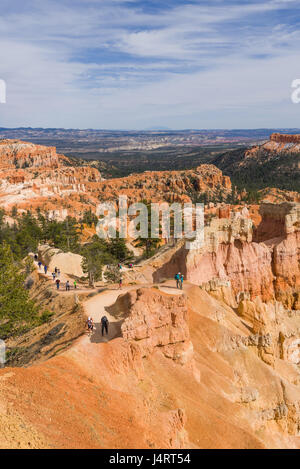 Persone che camminano giù per un sentiero tra le rocce di arenaria hoodoo pilastri in all'Anfiteatro del parco nazionale di Bryce Canyon, Utah Foto Stock