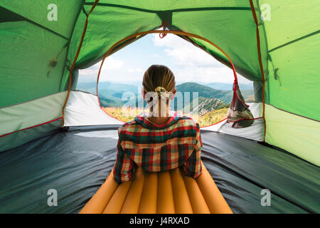Ragazza seduta in essi tenda contro lo sfondo di un incredibile paesaggio di montagna. Giornata di sole in highland Foto Stock
