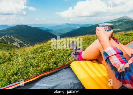 Ragazza seduta nella loro tenda con tè caldo contro lo sfondo di un incredibile paesaggio di montagna. Giornata di sole in highland