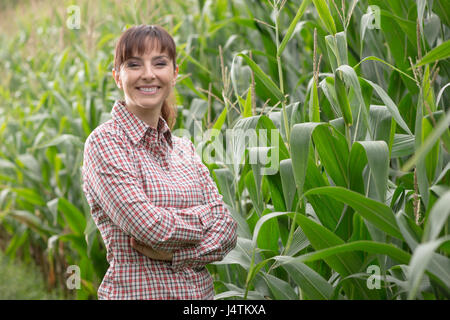 Femmina allegro l'agricoltore e imprenditore in posa il raccolto di mais e sorridente alla fotocamera, agricoltura e concetto di coltivazione Foto Stock