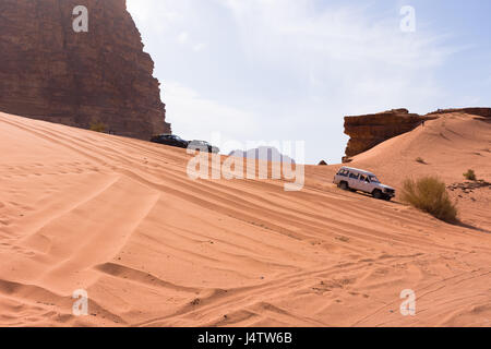 Quattro Wheeling in Wadi Rum giù un arance grandi dune di sabbia con montagne rocciose in background e cielo blu con nuvole sottili sopra. Foto Stock