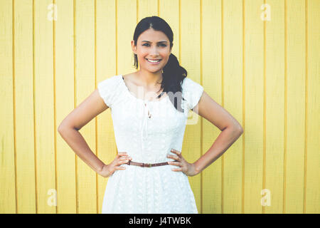 Closeup ritratto, felice successo fiduciosa piuttosto giovane donna in abito bianco con le mani sui fianchi, isolato su sfondo giallo . Positivo emot umana Foto Stock