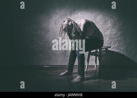 Triste giovane donna seduta da sola in una sedia in una stanza vuota Foto Stock