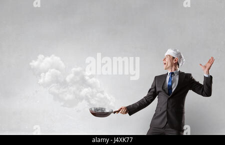 Giovane uomo nel business suit e cuocere hat holding pan. I supporti misti Foto Stock