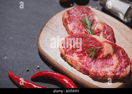 Carne di manzo crudo su un tagliere con le spezie e gli ingredienti per cucinare. Foto Stock