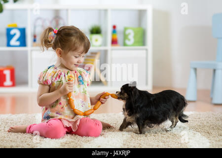 Bambino ragazza salsicce di alimentazione al suo cane sul pavimento in vivaio. Foto Stock