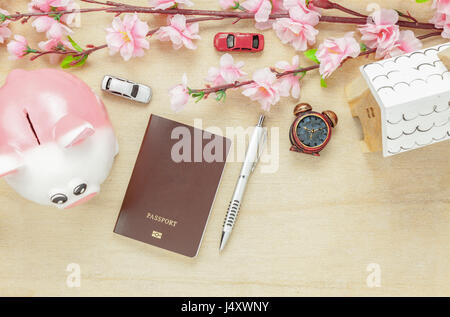Vista dall'alto ufficio business desk concetto. Risparmio di denaro per viaggiare con il passaporto.casa in legno anche auto e orologio sul ripiano di legno.Il bellissimo fiore rosa w Foto Stock
