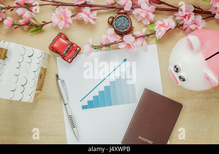 Vista dall'alto ufficio business desk concetto. Risparmio di denaro per viaggiare con il passaporto.Riepilogo inseriti con casa in legno anche auto e orologio sul ripiano di legno.be Foto Stock