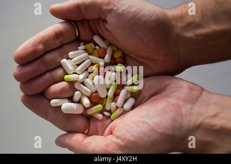 Uomo con un mucchio di compresse, capsule e confetti nel palmo della mano Foto Stock