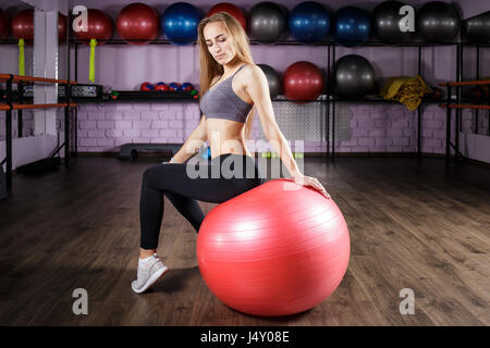 Giovane bella ragazza fitness seduti sulla sfera di fitness nel club salute. Bionda donna sportiva in palestra Foto Stock