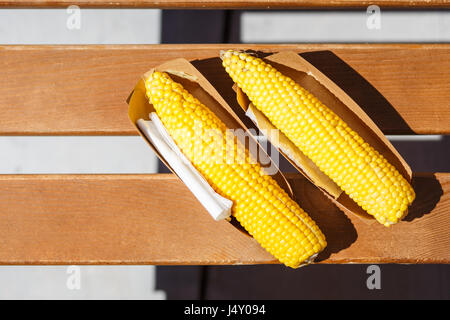Due bolliti salati sulla pannocchia di mais in scatola di carta. Spiaggia il fast food sfondo vista superiore Foto Stock