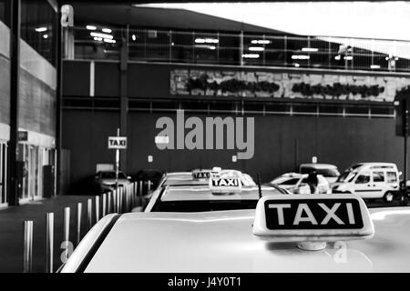 Una fotografia in bianco e nero di un taxy luci su tetto auto parcked in una riga nella parte anteriore della stazione dei treni di Milano città Foto Stock