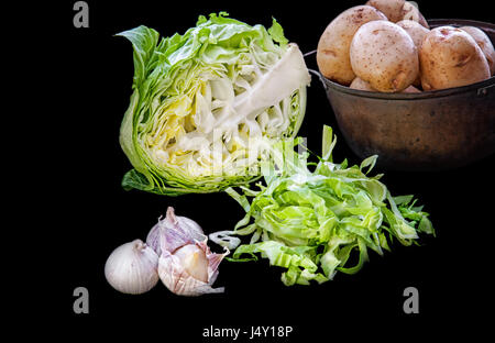 Cavolo verde metà metà testa tagliata a strisce per un insalata con le patate in una pentola e capi di aglio su un isolato nero lo sfondo. Il telaio orizzontale. Foto Stock