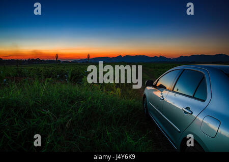 Auto sulla strada di campagna del settore agricolo con un bellissimo tramonto Cielo Foto Stock