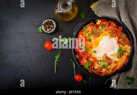 La prima colazione. Uova fritte con verdure - shakshuka in una padella su uno sfondo nero in stile turco. Lay piatto. Vista superiore Foto Stock