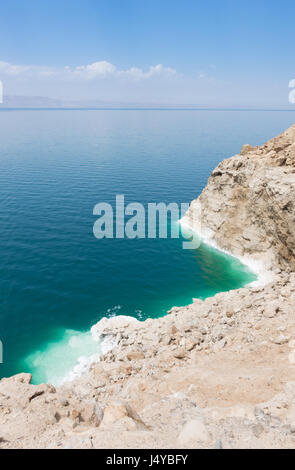 Affacciato sul Mar Morto con il suo colore turchese e acquamarina acqua e robusto, in crosta di sale di banca. L'orizzonte è opaco con cielo blu e nuvole sopra. Foto Stock